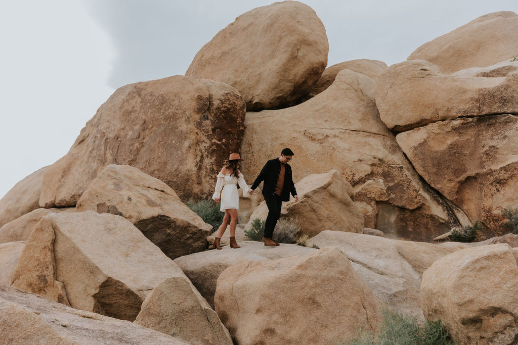 Desert boho engagement session with couple holding hands and walking down desert rock together