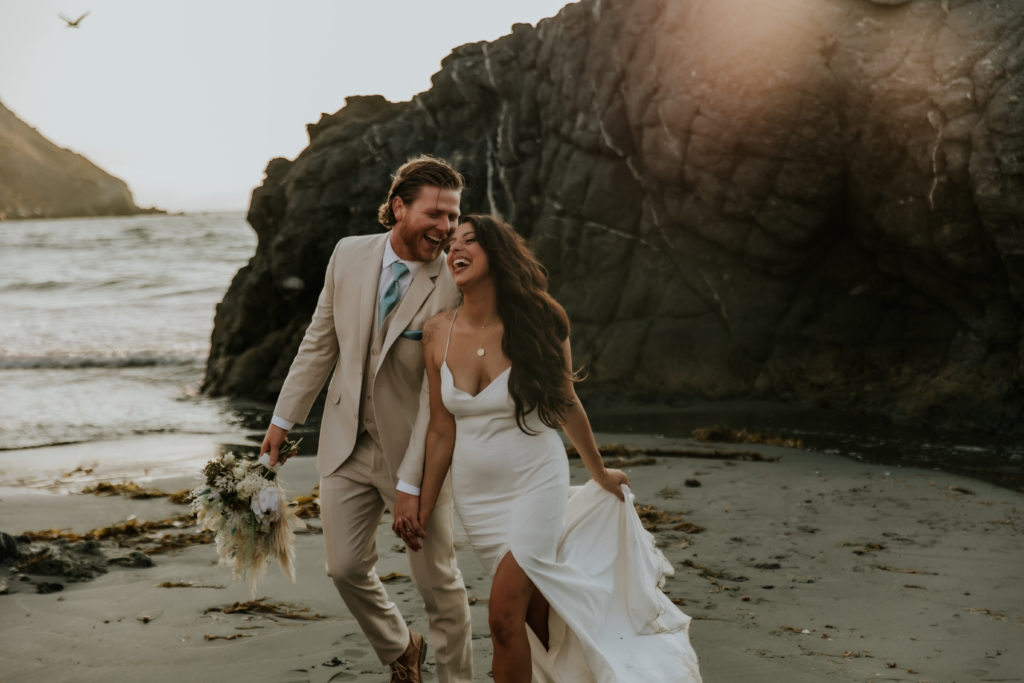 Bride Laughing while walking on the beach with groom