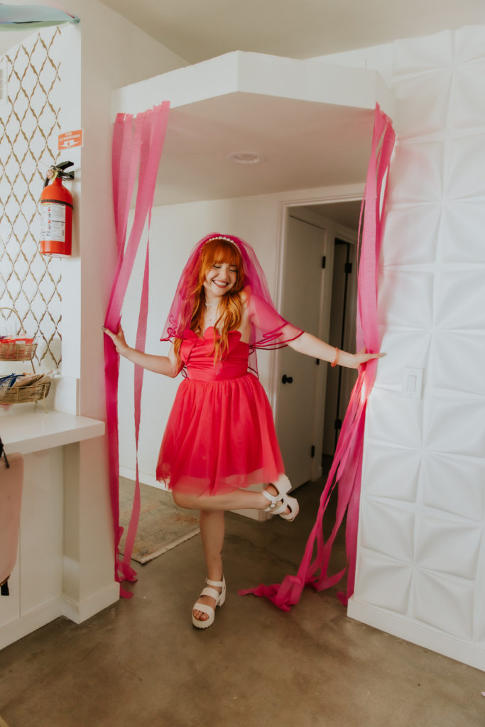 Bride walking through doorway with pink streamers at her bachelorette party
