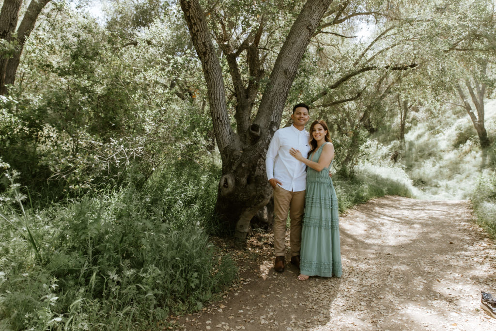 Cute couple in a forest smiling at the camera during their engagement photos