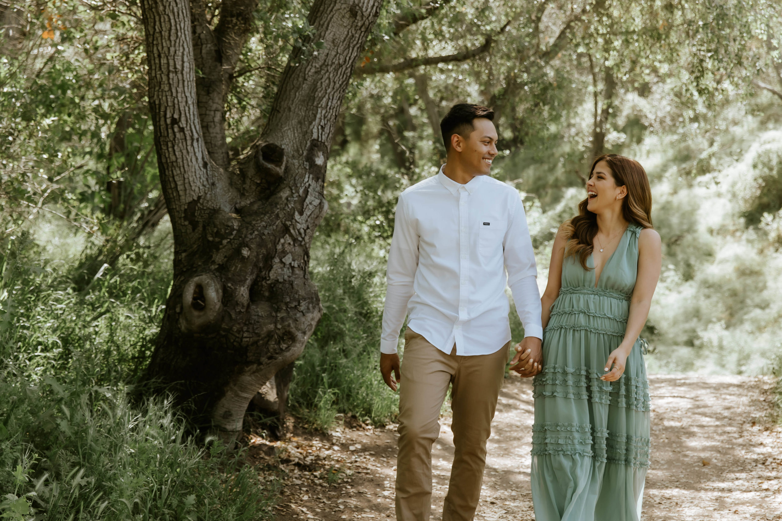 couple laughing during their engagement photoshoot while walking under some trees