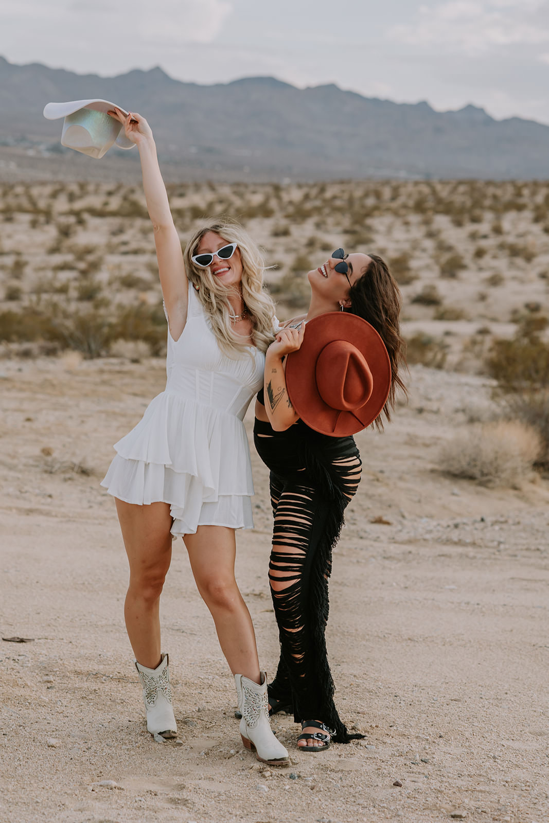 bride throwing cowboy hat in the air while posing with her bridesmaid in the desert during her bachelorette party