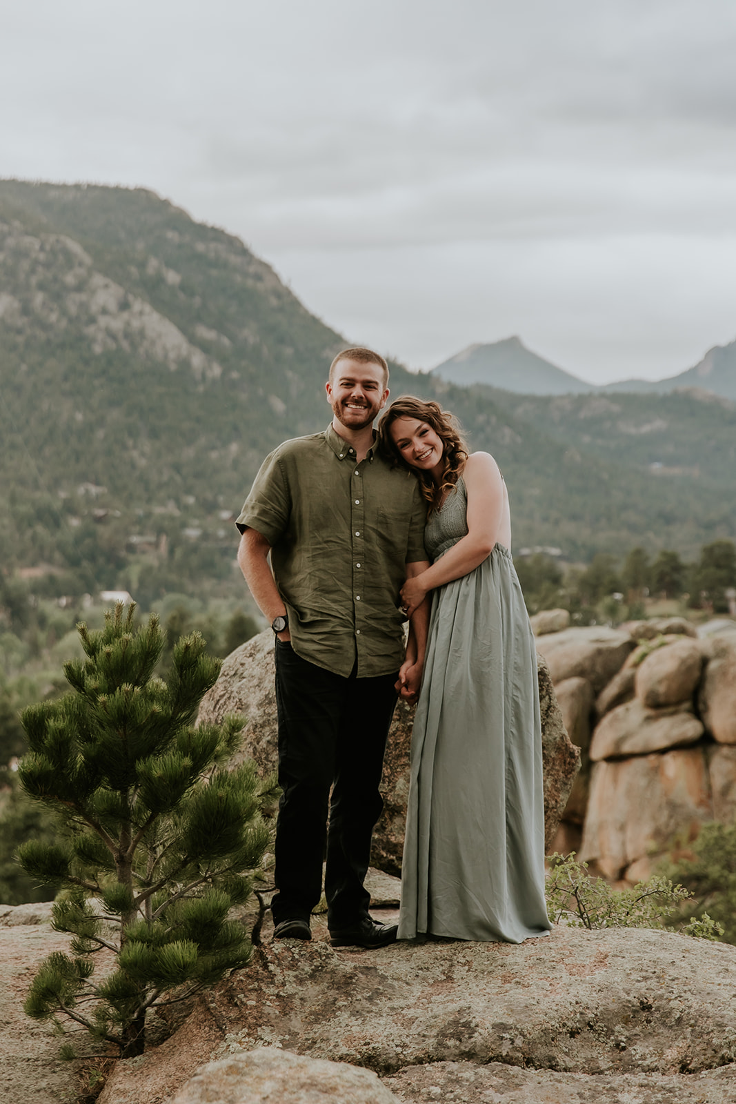 couple holding hands standing on a rock with the rockies in the background