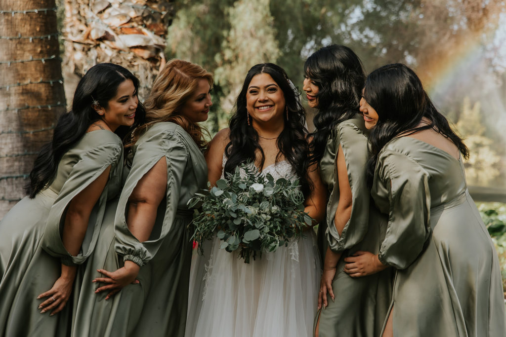 bride and bridesmaids smiling at eachother with a rainbow in the backgrounnd