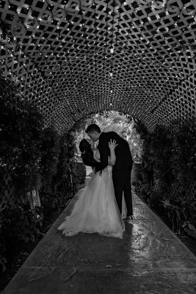groom kissing bride and dipping her back under a light up tunnel