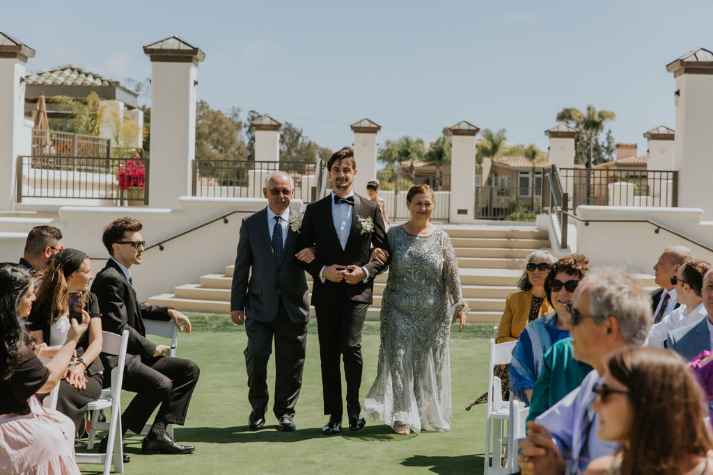 Groom walking down the aisle with his parents at the Marbella Country Club in San Juan Capistrano
