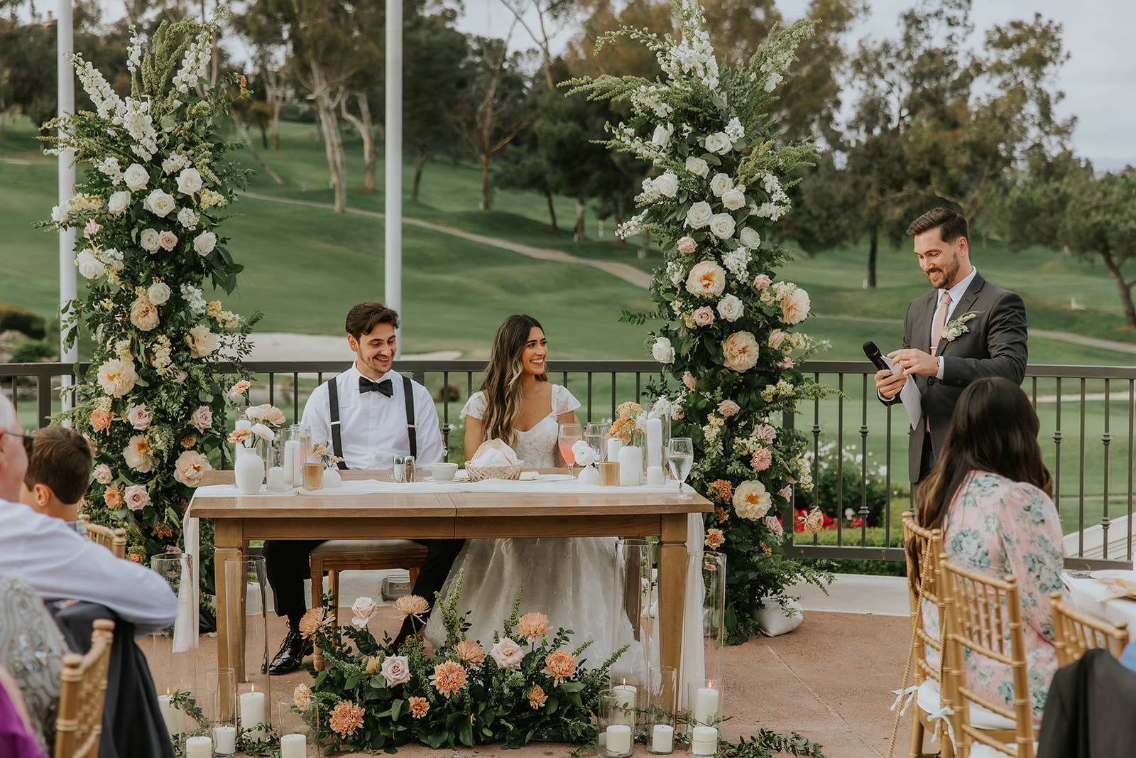 Groom and Bride sitting at the head table with the floral arch behind them