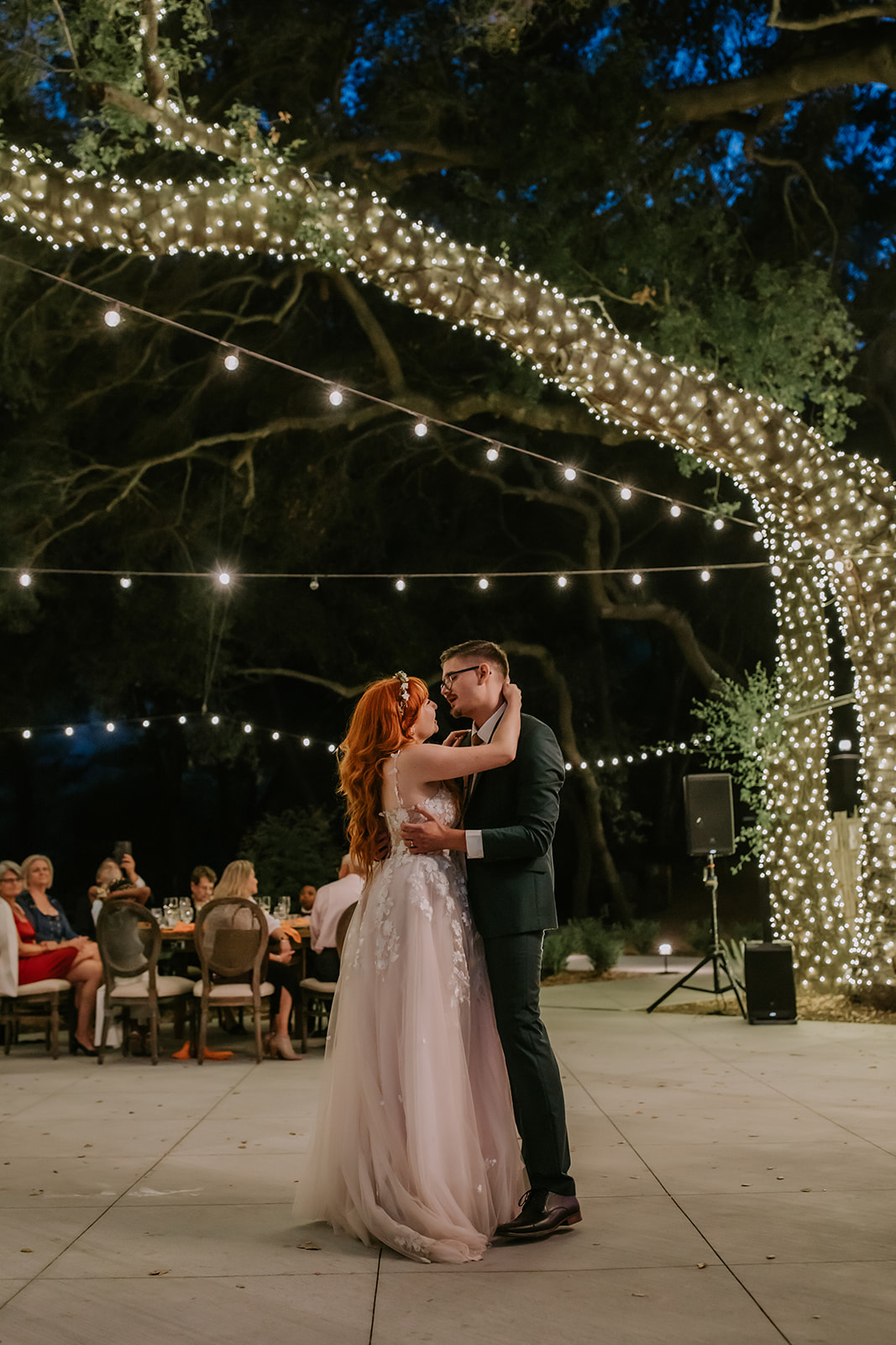 bride and groom sharing their first dance on the patio at the oaks at duncan lane surronded by oak trees wrapped in string lights