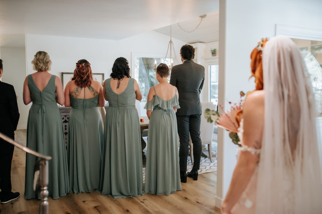 bride facing her bridal party that is turned away from her so she can surprise them with how she looks