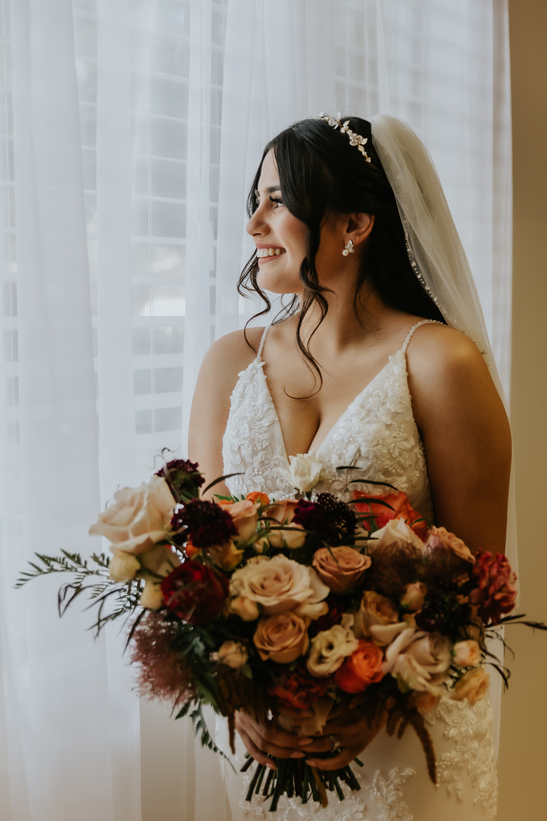 portrait of bride holding her bouquet looking out the window with her veil on