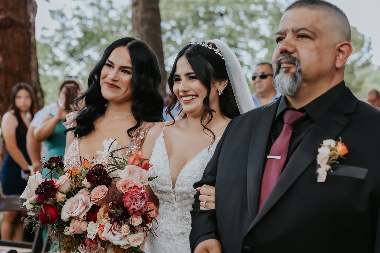 Bride smiling at the groom while walking down the aisle with her parents