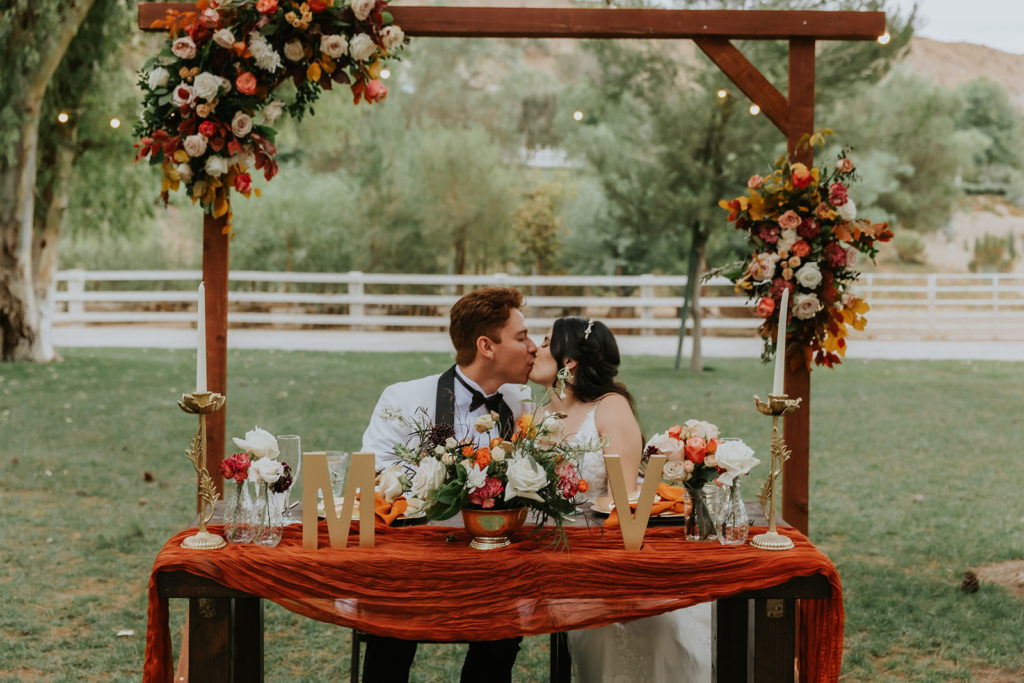 bride and groom kissing at the head table during their reception at their 70s themed wedding