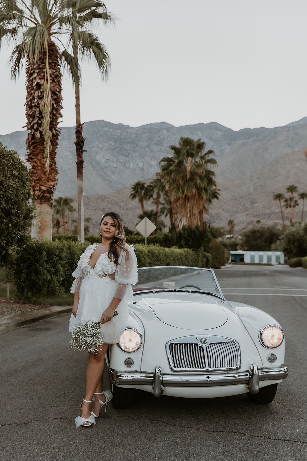 newly engaged women leaning on a classic car in palm springs during her engagement session with her fiance