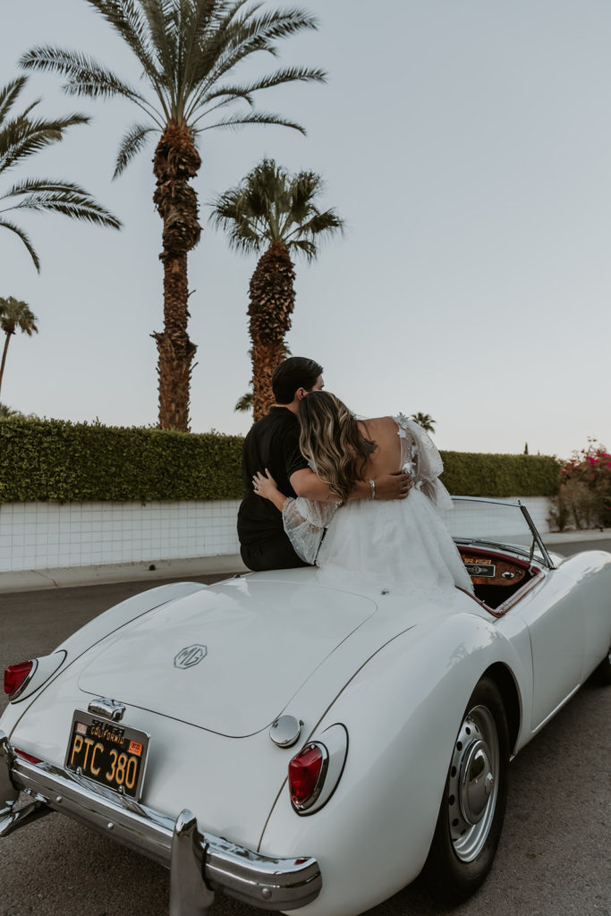 newly engaged couple sitting on the tops of seats in a classic car with them facing away from the camera during their engagement photos in indian canyon
