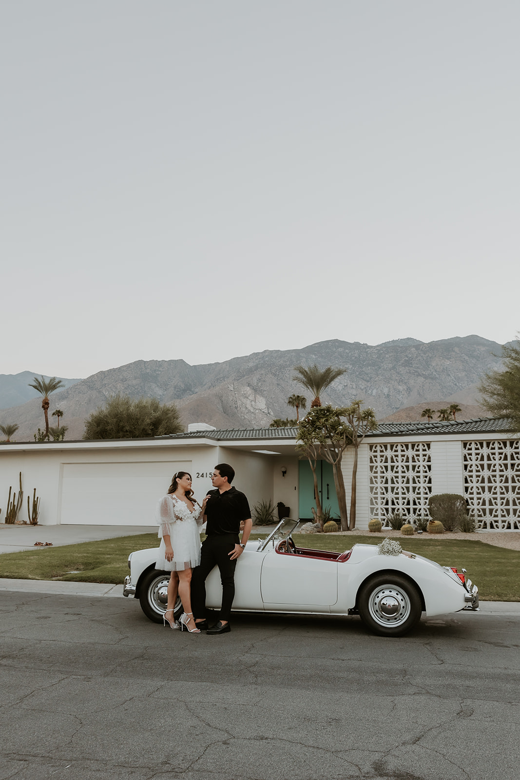 newly engaged couple leaning on a classic car in palm springs during their engagement session