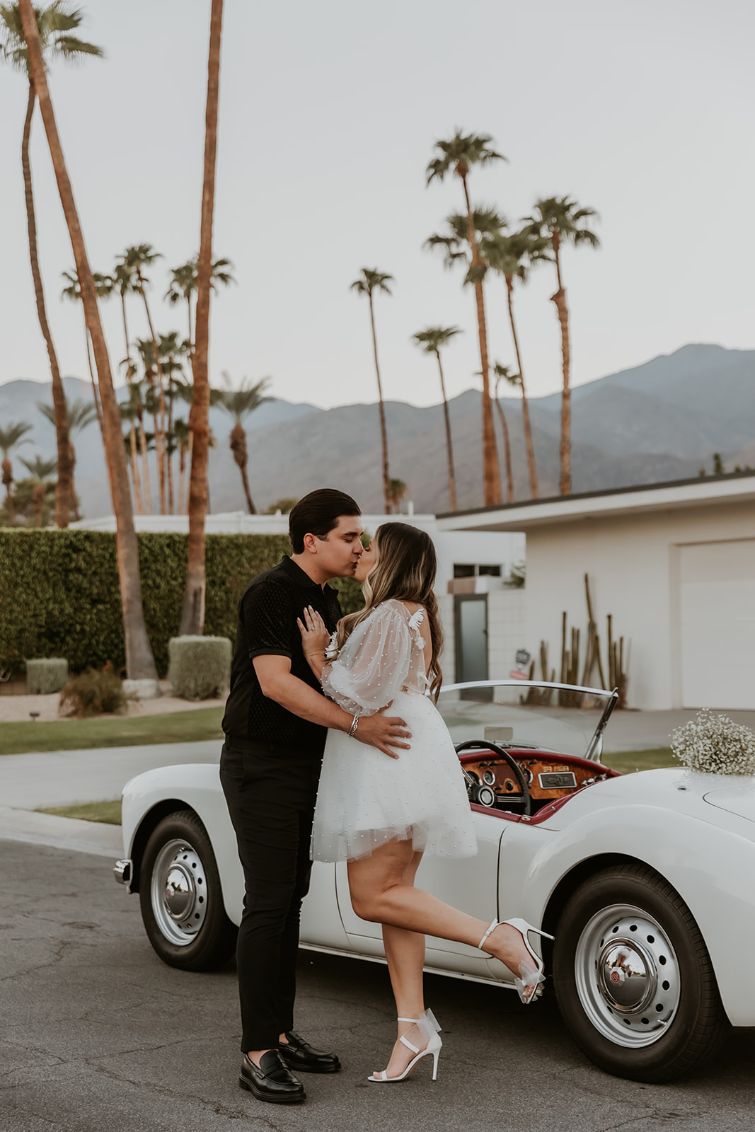newly engaged couple kissing in front of a classic car in palm springs