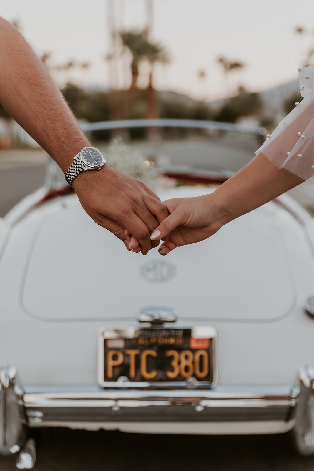 hands of a newly engaged couple showcasing an engagement ring and classic car in the background