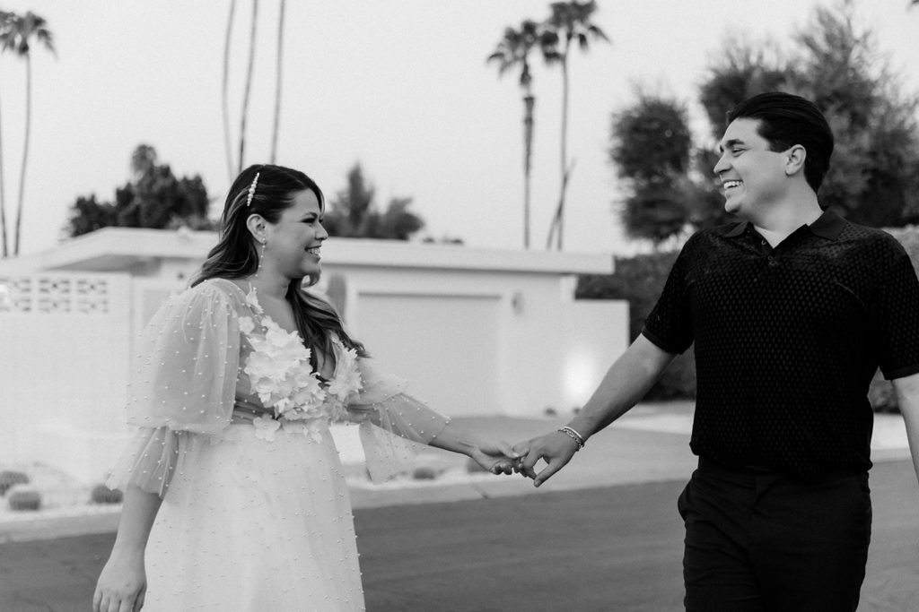 black and white photo of a newly engaged couple smiling at each other and walking down the street holding hands