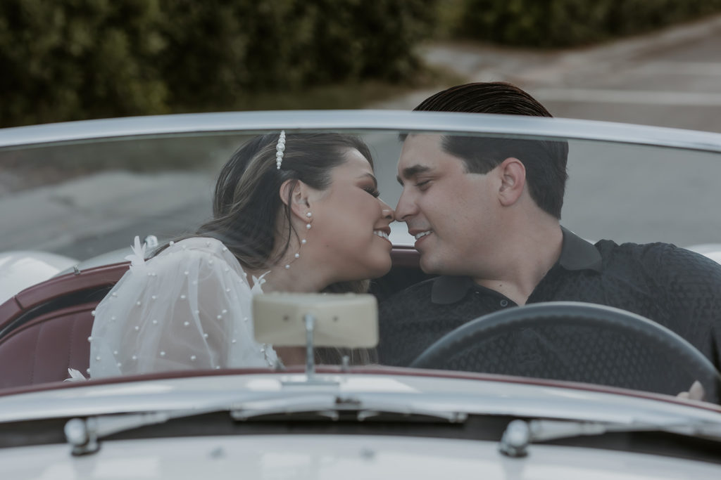 newly engaged couple sitting in a classic car smiling at each other with the camera shooting through the windshield